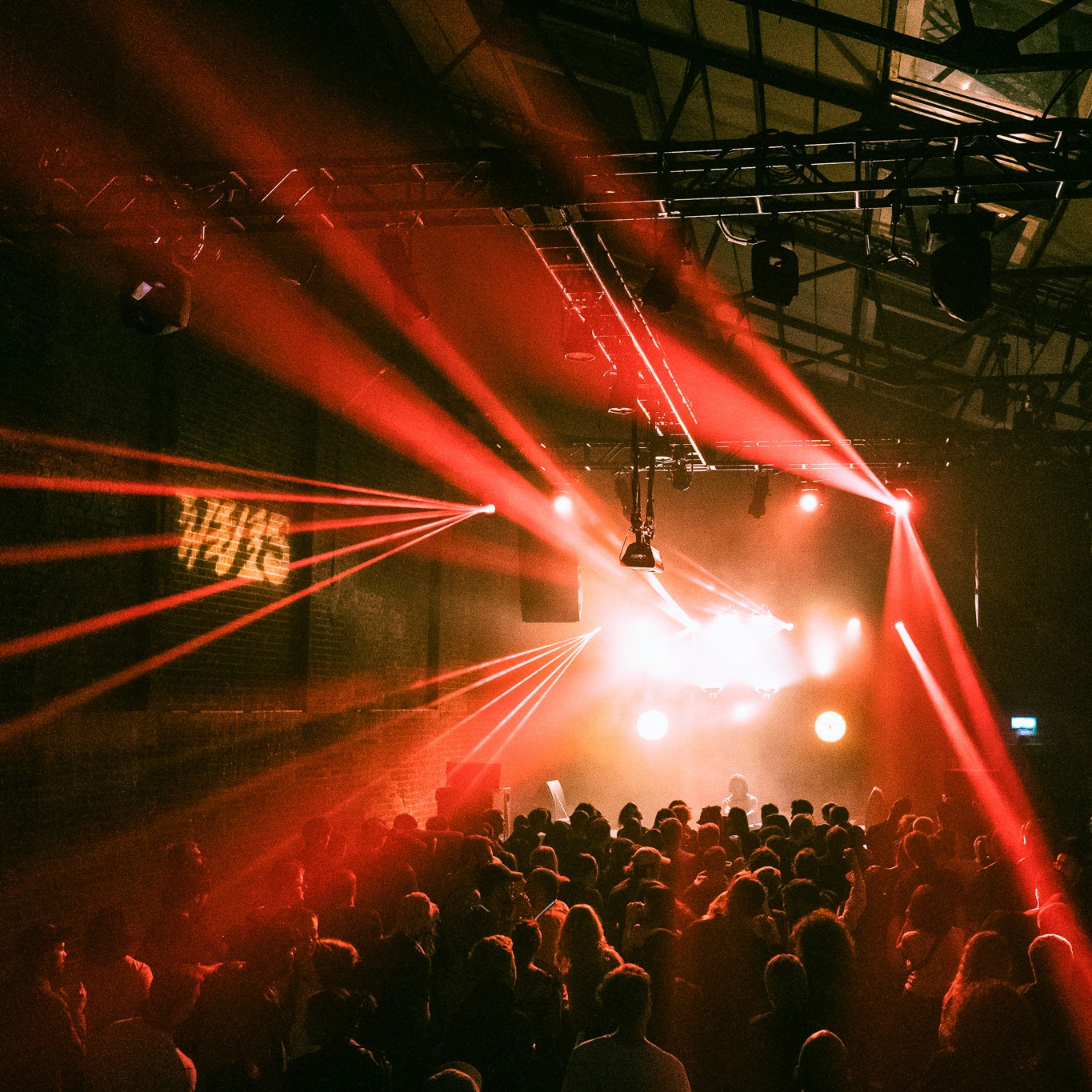 A photo of Village Underground from the back of the venue, showing its warehouse-style interior, a crowd watching a DJ and red beaminig lights shooting towards the camera